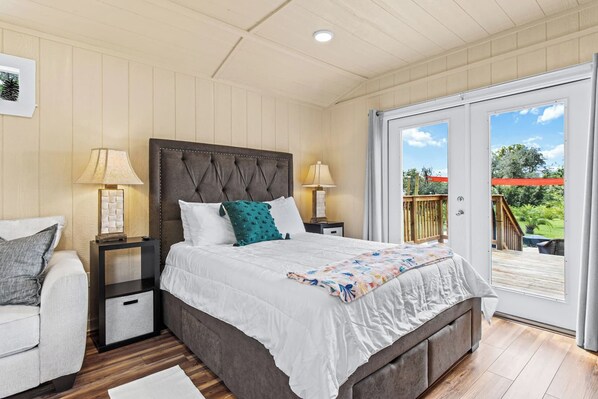 A bedroom with a large bed, two bedside tables, a nightstand, a chair, and a sliding glass door leading to an outdoor area.