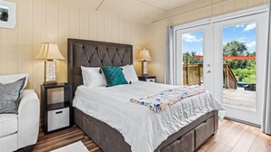 Un dormitorio con una cama grande, dos mesitas de noche, un pequeño mueble auxiliar, un sofá y un ventanal corredero a una terraza.