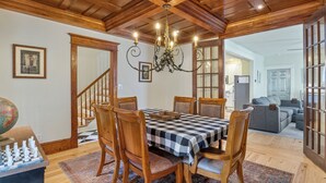Un comedor con mantel a cuadros, sillas de madera, una araña y un tablero de ajedrez.