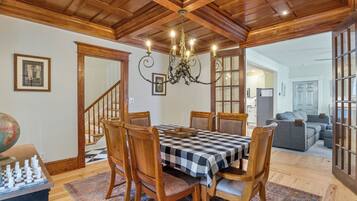 A dining area with a checkered tablecloth, wooden chairs, a chandelier, and a chessboard.