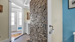 Un pasillo con piso a cuadros, pared de piedra, puerta blanca y pared azul con un cuadro enmarcado.