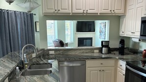 A modern kitchen with white cabinets, a stainless steel dishwasher, a black coffee maker, and a large window with blinds. - Lakefront home away from home! (Hot Springs)