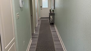 A hallway with a patterned rug, a door at the end, and a wall-mounted security device. - Lakefront home away from home! (Hot Springs)