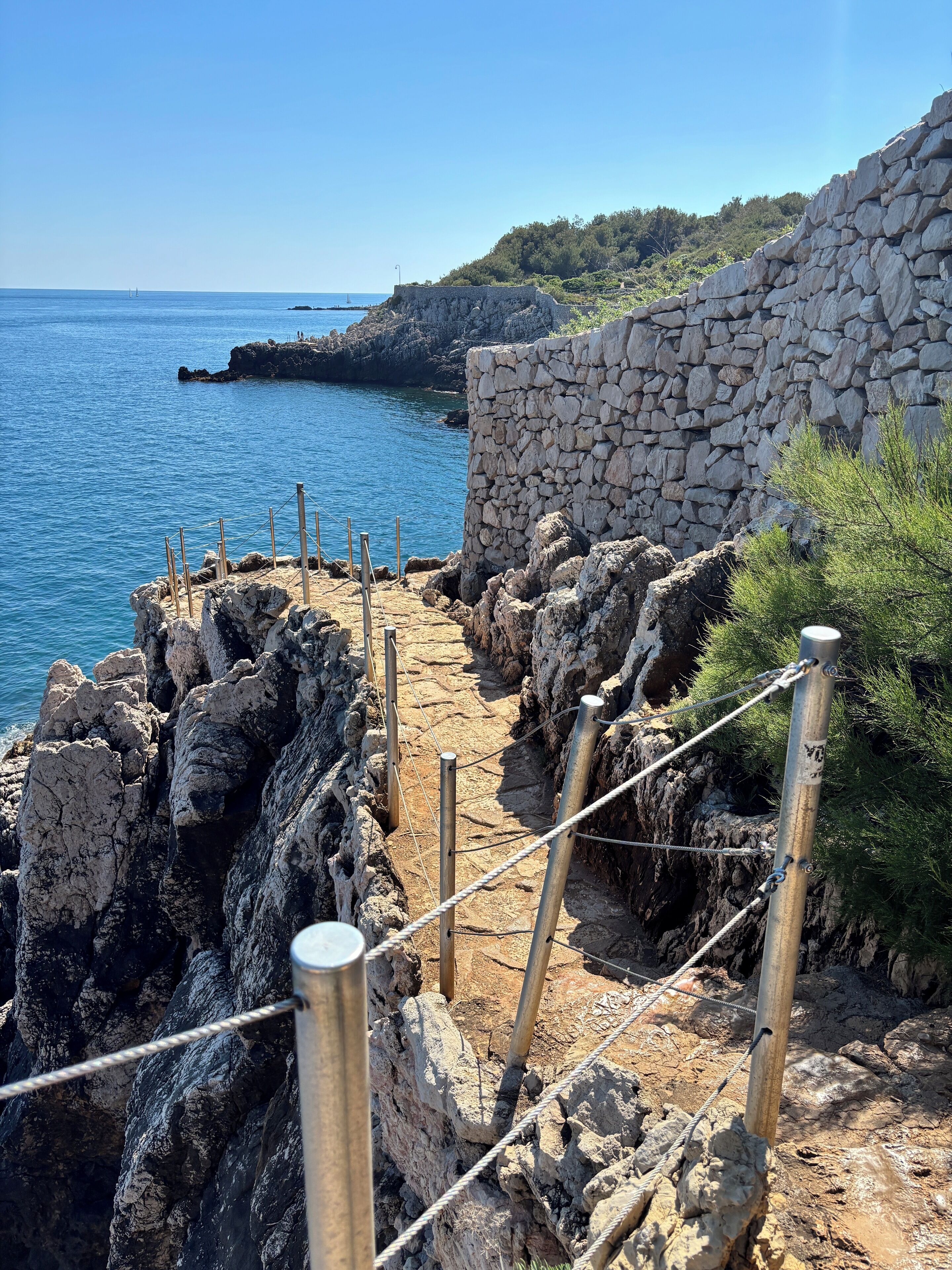 Un sendero de piedra costero que conduce a un afloramiento rocoso con vistas despejadas al mar.