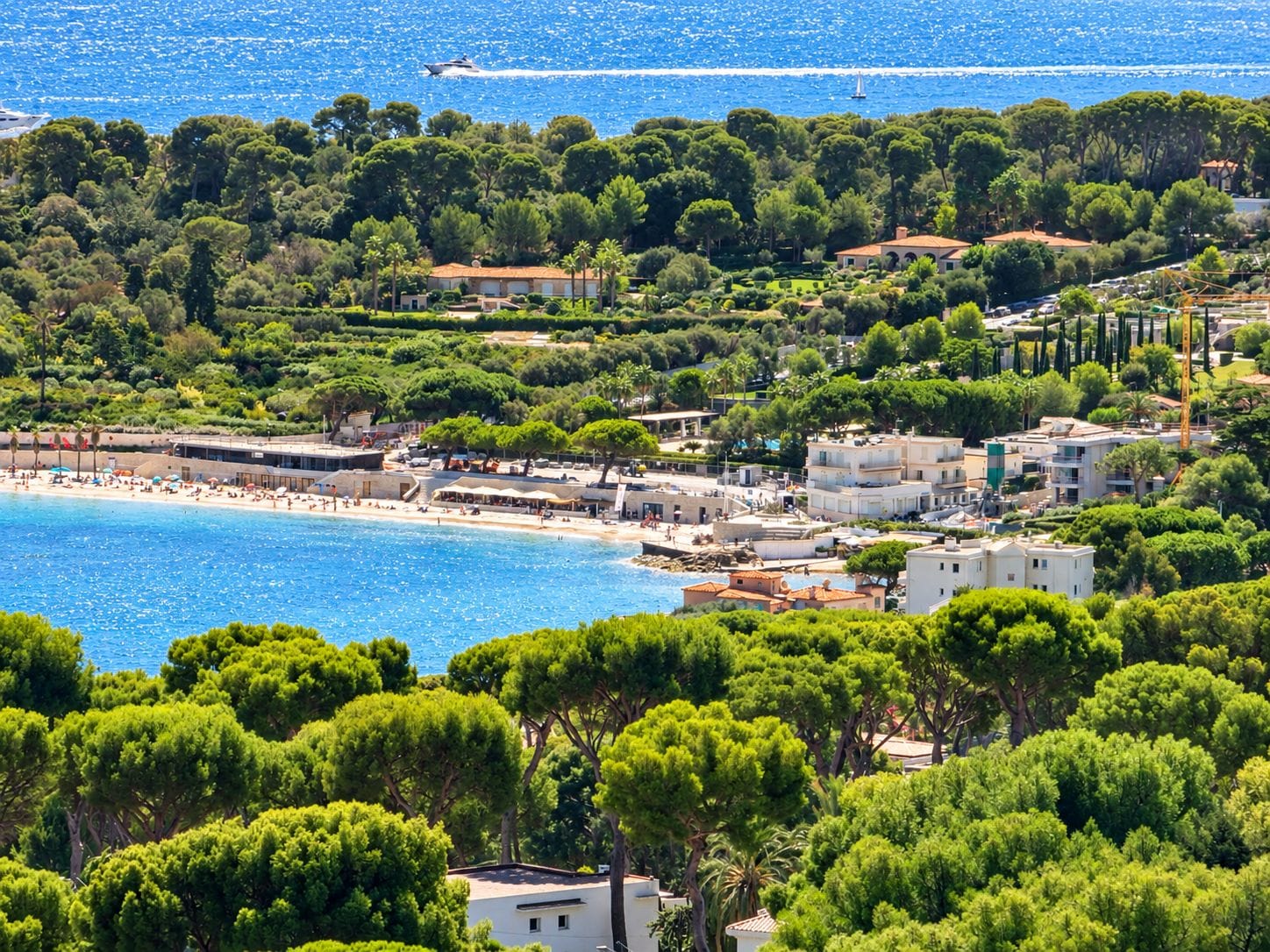 A coastal area with a beach, buildings, and dense greenery.