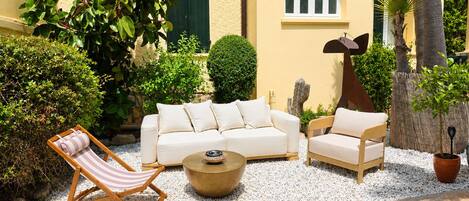 A patio with a white sofa, two armchairs, a small table, and a striped lounge chair.