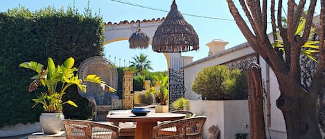 Un patio exterior con mobiliario de mimbre, una mesa redonda y lámparas de paja colgantes.