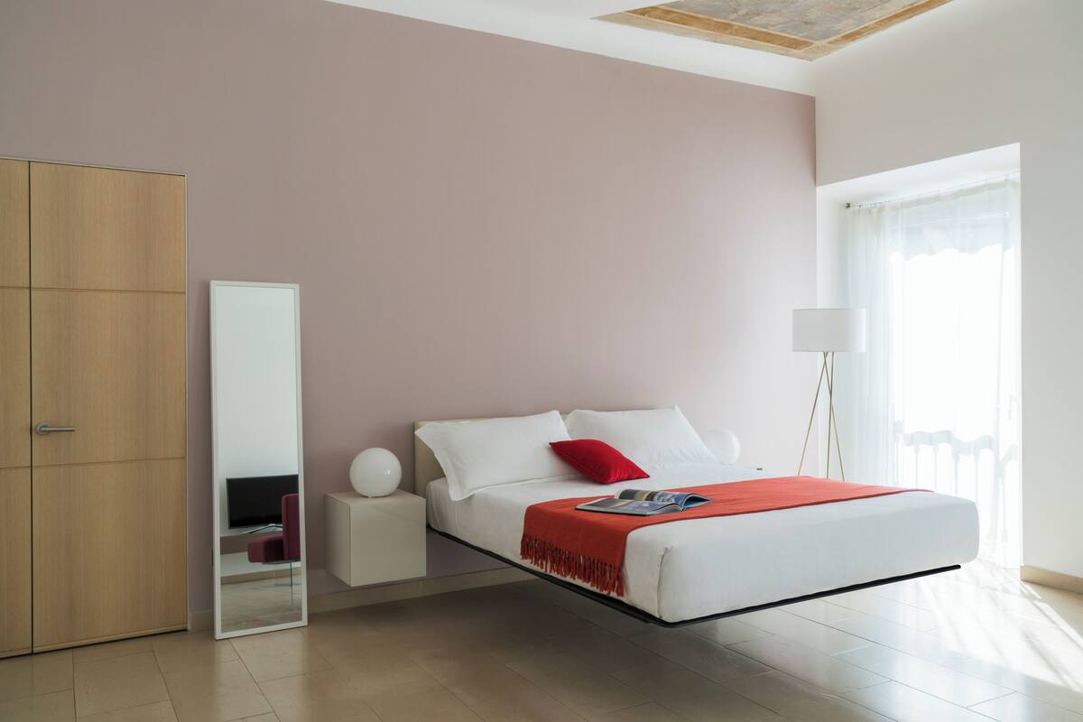 Een moderne slaapkamer met een bed, een garderobe, een nachtkastje, een spiegel en een vloerlamp.