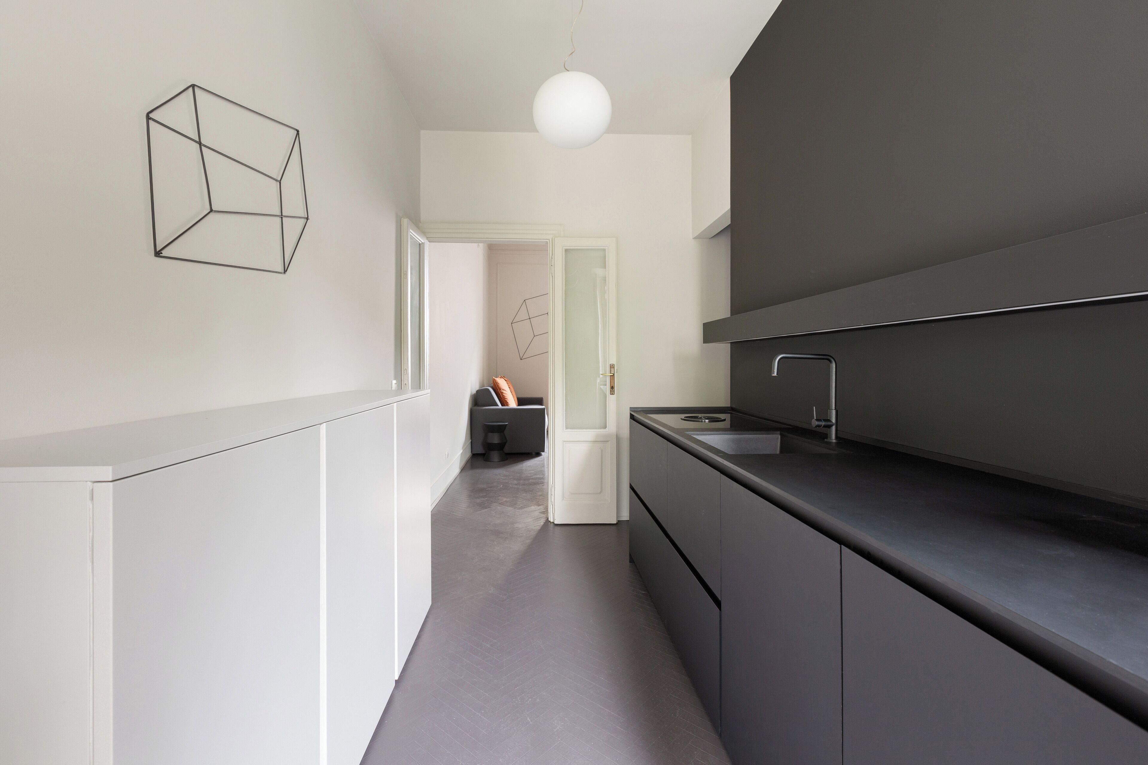 A modern kitchen with a dark countertop, white cabinets, and a geometric wall art piece.