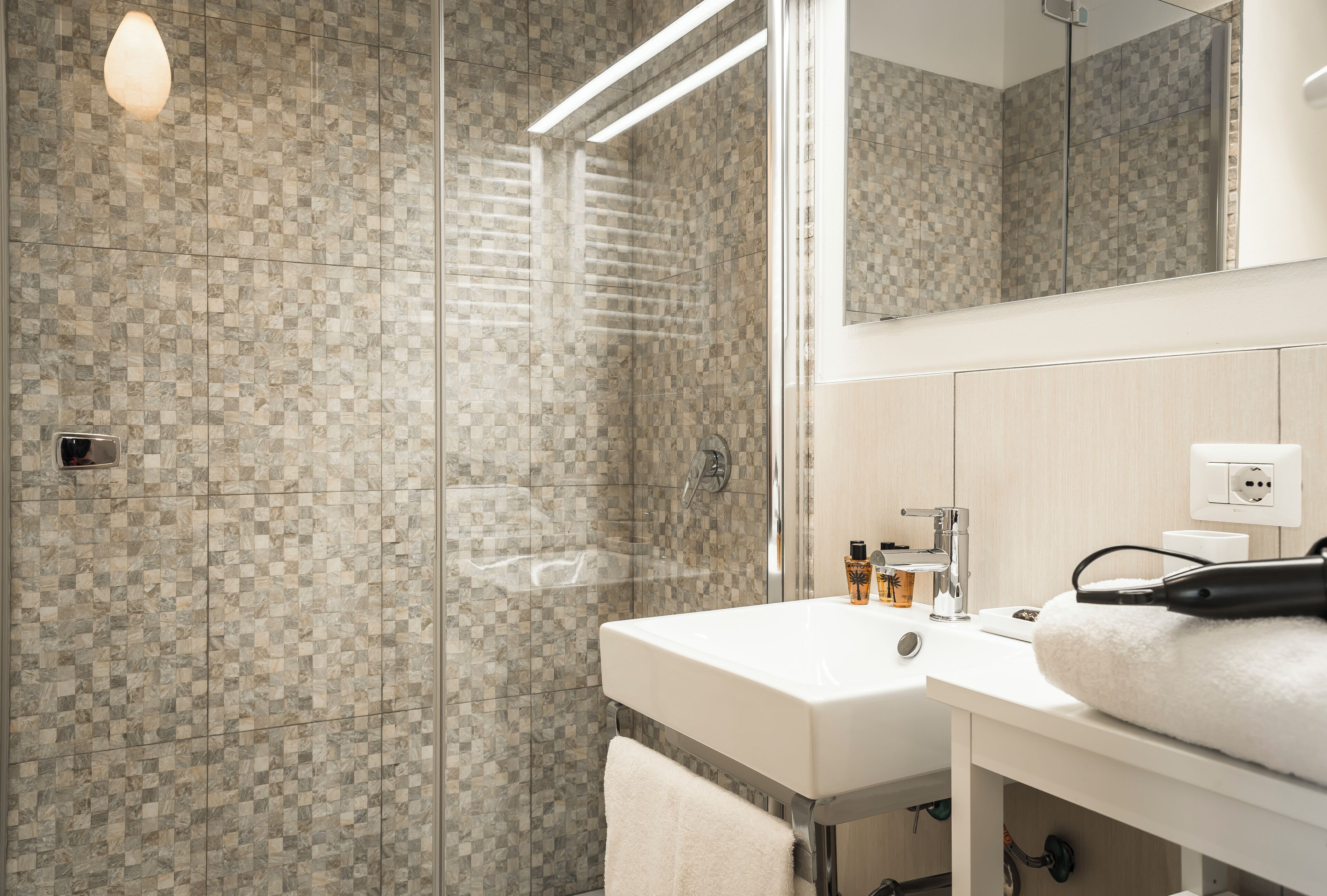 A modern bathroom with a glass shower enclosure, a white sink, and a mirror above it.