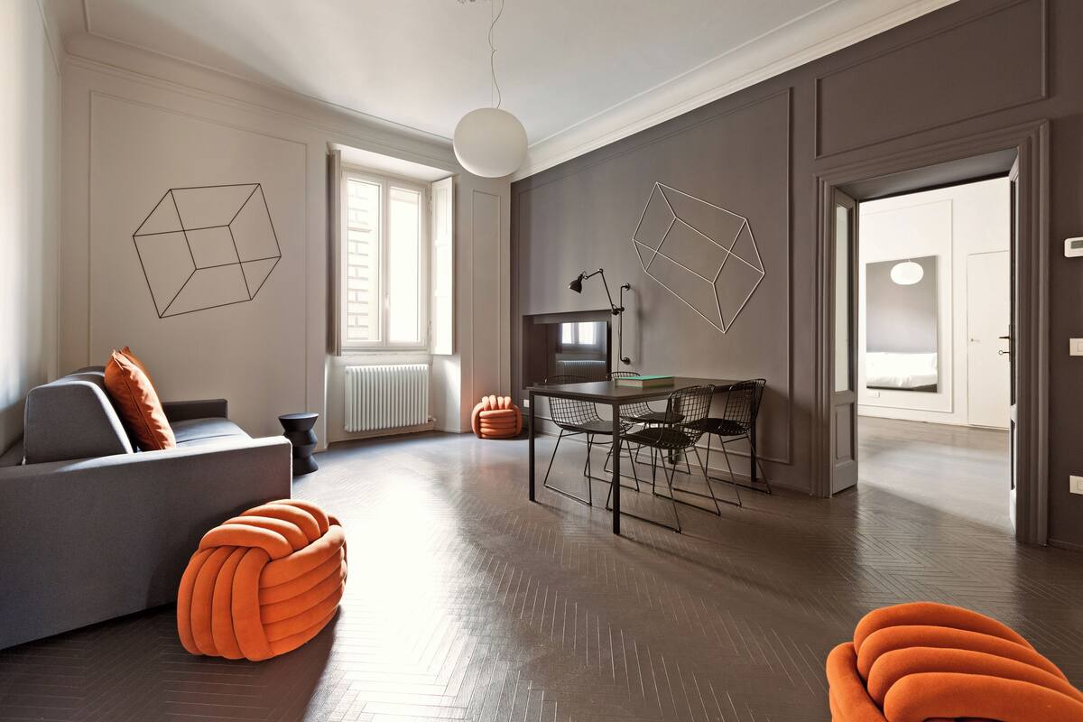 Een moderne woonkamer met een bank, een oranje poef, een eettafel en stoelen.