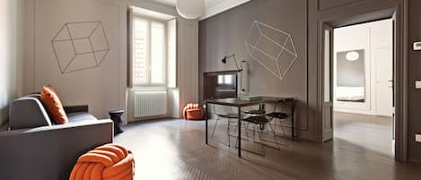 A modern living room with a sofa, orange ottoman, dining table, and chairs.