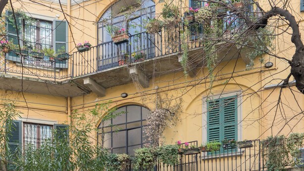 A multi-story building with balconies, large windows, and potted plants. - Brera Apartments in Porta Volta (Milan)