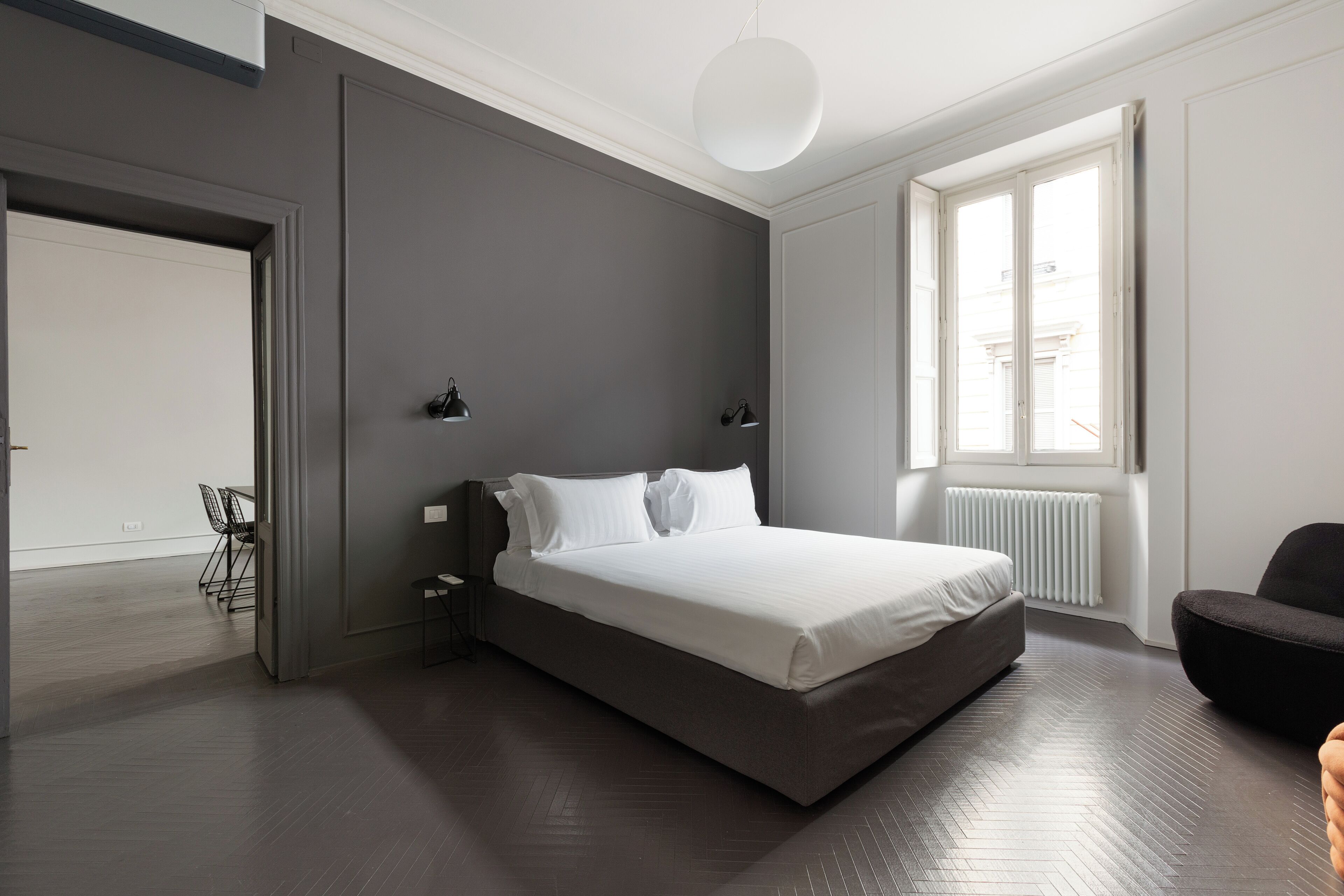 Una camera da letto moderna con un letto grande, comodini, una sedia e una finestra che lascia entrare luce naturale.