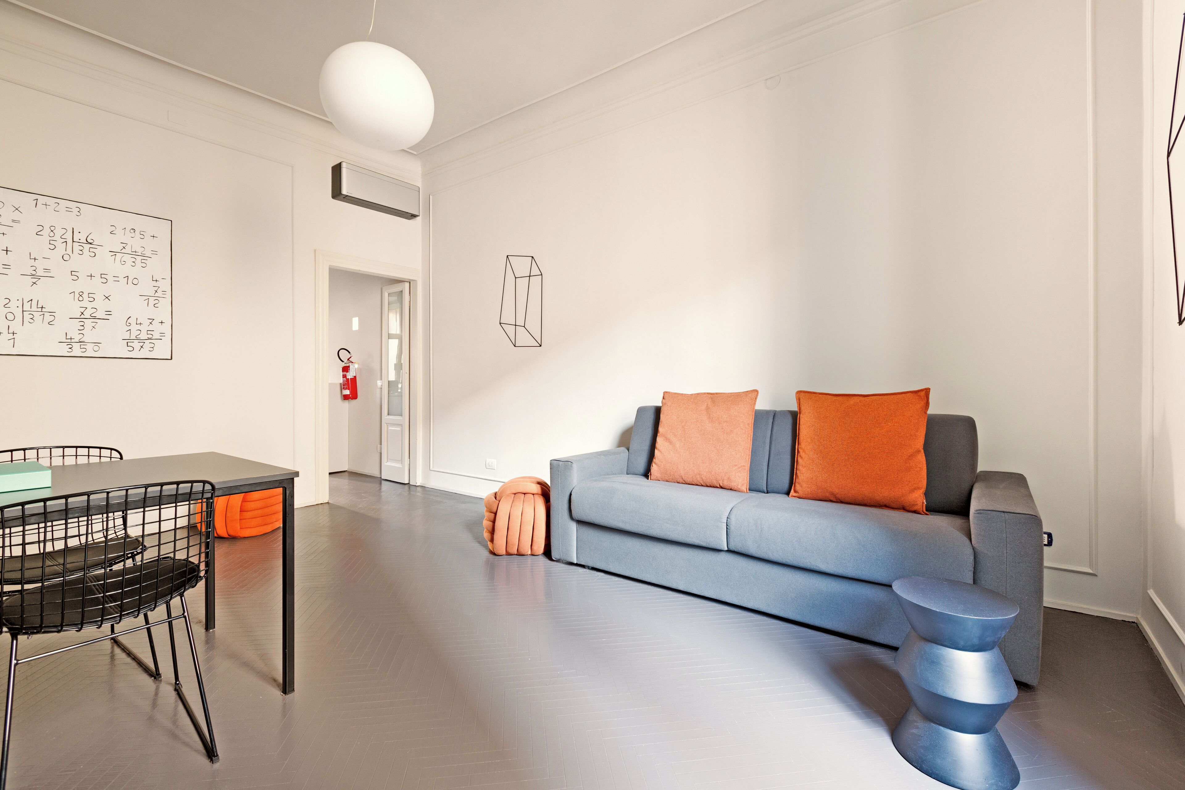 A modern living room with a grey sofa, orange cushions, a black chair, and a small side table.