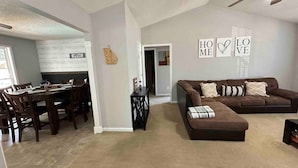 A living room with a brown sectional sofa, a dining table with chairs, and a kitchen area in the background. - Beautiful Ranch Style House With Pool (Aragon)