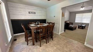 A dining area with a wooden table set for four, a black and white accent wall, and a ceiling fan. - Beautiful Ranch Style House With Pool (Aragon)