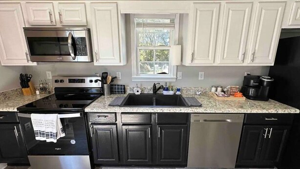 A kitchen with white upper cabinets, a stainless steel microwave, a black stove, a sink, and a dishwasher. - Beautiful Ranch Style House With Pool (Aragon)