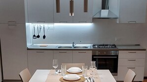 Une cuisine moderne avec des meubles blancs, une table à manger pour quatre personnes et des luminaires suspendus.