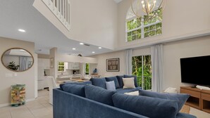 A modern living room with a blue sectional sofa, a flat-screen TV, and a kitchen in the background.