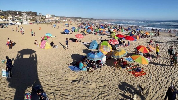 Una playa concurrida con numerosos paraguas de colores y gente disfrutando del clima soleado.