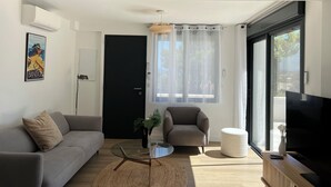 A modern living room with a grey sofa, a round glass coffee table, a grey armchair, and a TV on a wooden stand.