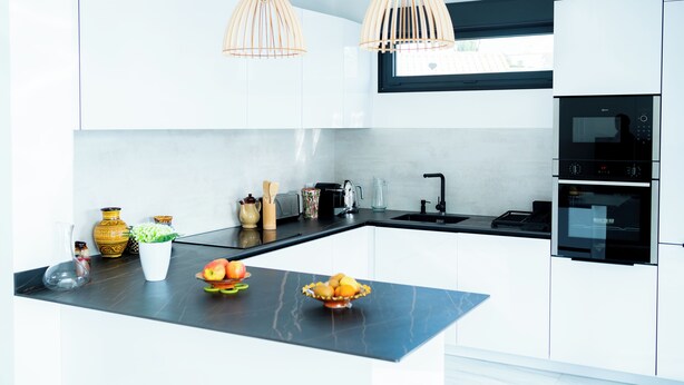 A modern kitchen with white cabinets, a black countertop, and two pendant lights.