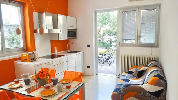 Una cucina moderna con mobili bianchi e un'area pranzo con sedie e tavolo arancioni.