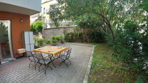 Una veranda esterna con tavolo apparecchiato per quattro persone, circondata da sedie, in zona residenziale con muro in pietra e vegetazione.