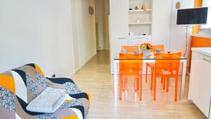 Un soggiorno moderno con un divano, un tavolo da pranzo con sedie e un angolo cucina con televisore.