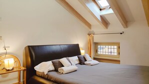 Une chambre à coucher avec un grand lit, une table de chevet avec une lampe, une fenêtre avec des rideaux et un puits de lumière.