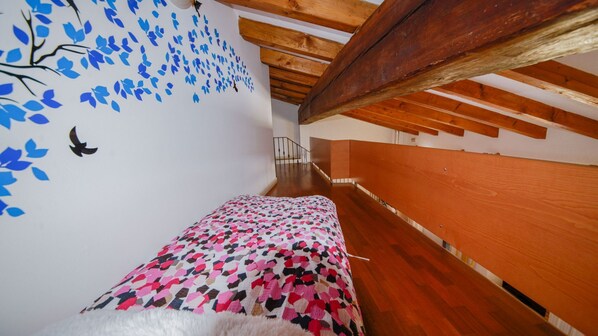 Una habitación estrecha con paneles de madera, un edredón estampado, y una pared decorada con motivos de hojas azules, además de una escalera que conduce a un nivel superior.