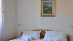 Een slaapkamer met een bed, kussens, een schilderij aan de muur en een deur.