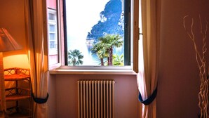 A room with a window overlooking a coastal view, a radiator, and a chair with a lamp.