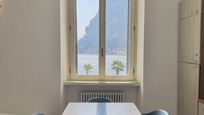 A room with a large window overlooking a body of water and a cliff. There is a table with chairs and a cabinet to the right.