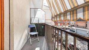 Ein Balkon mit blauem Stuhl, einem Metallgitter und Blick auf eine Straße mit parkenden Autos und Gebäuden.
