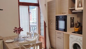 A compact kitchen with a washing machine, a small oven, and a dining area with a table and chairs. - One Bedroom Apartment (Riva del Garda)
