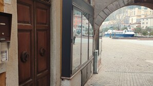 A stone archway leading to a cobblestone plaza with a view of a river and boats. - One Bedroom Apartment (Riva del Garda)
