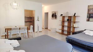 Une chambre d’hôtel moderne comprenant un lit, un bureau avec des chaises, une kitchenette et une bibliothèque.
