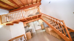Eine Holztreppe verbindet zwei Etagen, darunter befindet sich eine Küche.