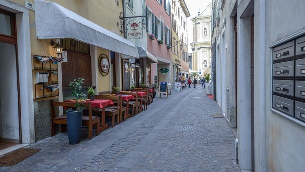 Eine enge Kopfsteinpflasterstraße gesäumt von Cafés mit Außenbestuhlung, jedes mit einer eigenen Markise und Beschilderung.