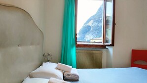 Ein Hotelzimmer mit Bett, Fenster mit Bergblick, Heizkörper und einem roten Sessel.