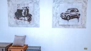 Zwei Wandbilder antiker Fahrzeuge, ein Kissen auf einer Holzkiste und ein Lichtschalter an der Wand.