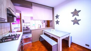 Une cuisine compacte avec une cuisinière à gaz, un banc en bois et une table à manger. Les murs sont décorés de motifs en forme d’étoile et il y a une fenêtre avec des rideaux.