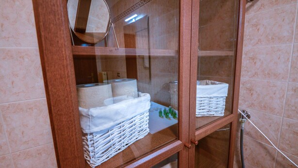 Baño con un mueble de madera que contiene papel higiénico y una cesta de mimbre.