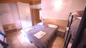 A bedroom with a bed, a bedside table, a wardrobe, and a radiator. - Two-Bedroom Apartment (Arco)