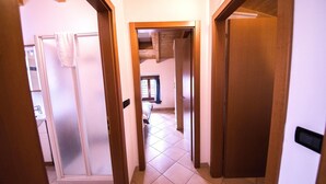 A hallway with wooden doors leading to a bedroom with a bed and a window. - Two-Bedroom Apartment (Arco)