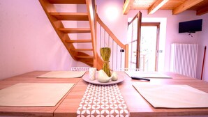 Una habitación con piso de madera, un futón de tatami, una mesa pequeña con un florero, un control remoto y un televisor en la pared.