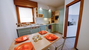 Een compacte keuken met turquoise kastjes, een eettafel voor vier personen en een raam met jaloezieën.