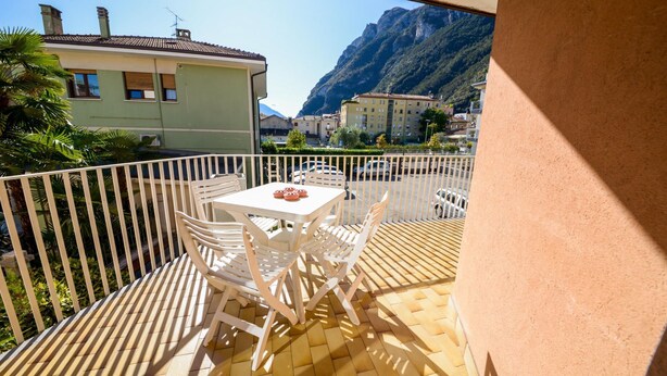 Een balkon met een tafel en stoelen, met uitzicht op een bergachtig landschap en een parkeerplaats.